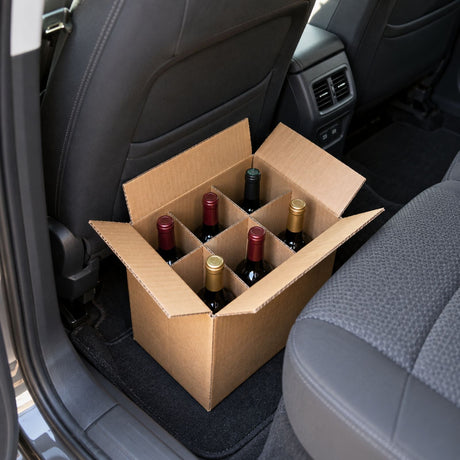 Carton ouvert à croisillons rempli de bouteilles de vin debout, posé sur le plancher arrière d’une voiture.